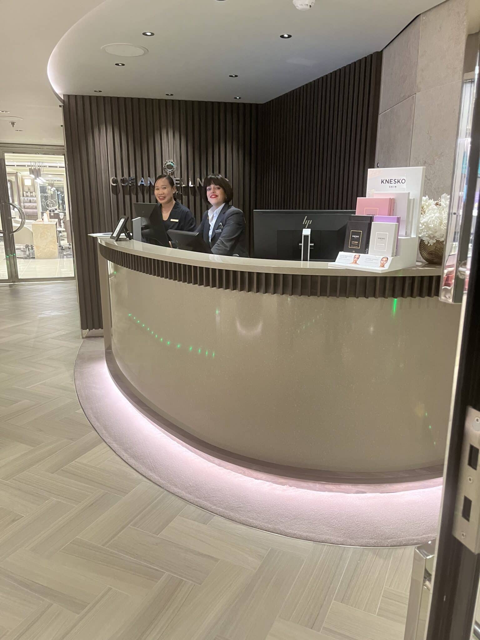 Ocean Wellness Spa reception desk with elegant curved design and two friendly staff members aboard Explora Journeys